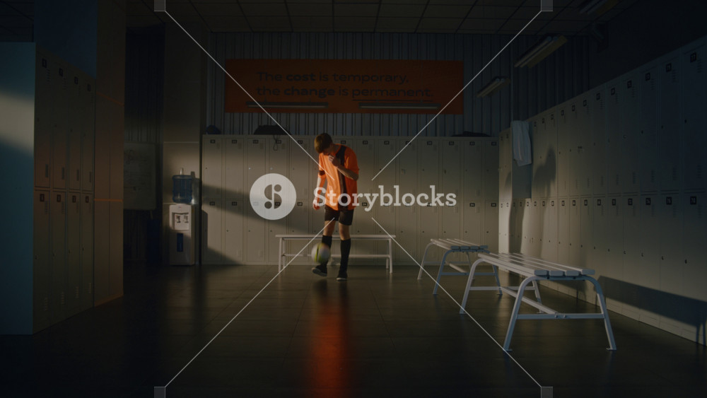 Talented Teenage Soccer Player in Orange and Black Kit Skillfully Juggling Football in Middle Empty Sports Dressing Room. Boy Maintains