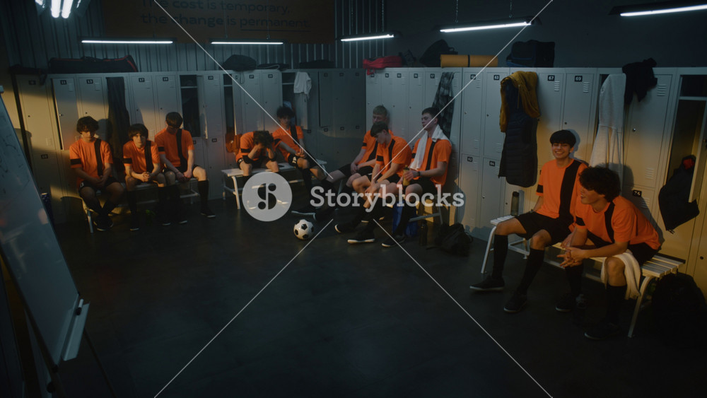 Coach Stands Before Group of Exhausted Teenage Football Players in Locker Room. Man Gestures, Expressing Disappointment and Critiquing