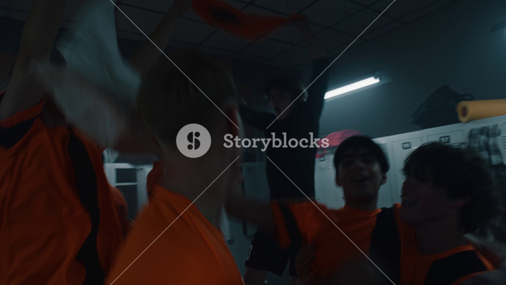 Thrilled Teenage Football Players Toss Teammate into Air, Celebrating Decisive Goal or Victory in Modern Locker Room. Concept of Triumph