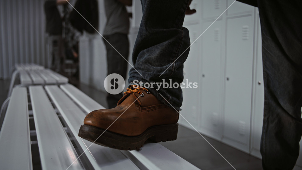 Close Up of Manual Laborer Resting Foot on Metal Bench, Carefully Tying Laces of Sturdy Protective Boots in Modern Warehouse or Factory