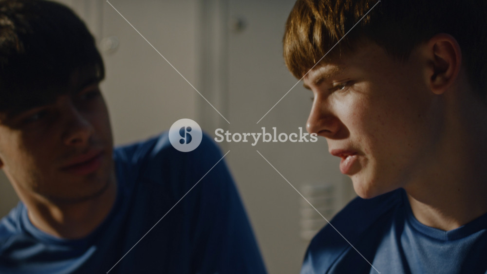 Candid Moment of Two Teenage Athletes Interacting in Industrial Style Locker Room. Boys Relaxed and Engaged in Casual Conversation
