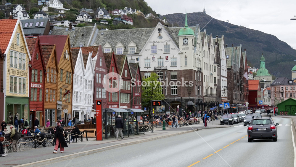 rows colorful wooden merchant houses cafes line busy street traffic moves past historic gabled buildings hillside homes bergens bryggen steady architecture