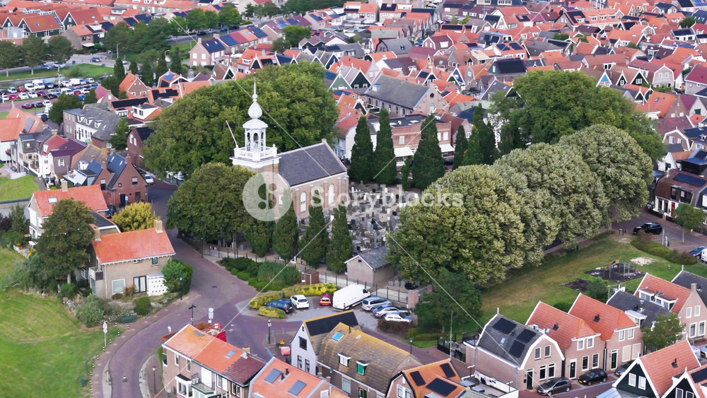 historic church prominent white bell tower stands beside tree lined cemetery signature orange roofed houses green spaces surround area urk netherlands orange-roofed