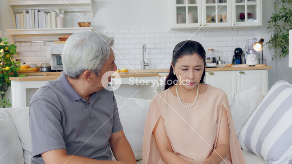 Asian elderly husband comforting upset wife crying with tears for problem. Attractive senior mature man support, consoling and understand empathy to depressed stressed woman in living room at home