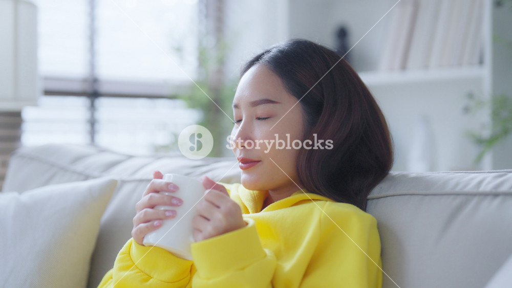 Young beautiful Asian woman her hands holding a cup of coffee morning winter time in living room. Happy and cheerful relaxing in winter