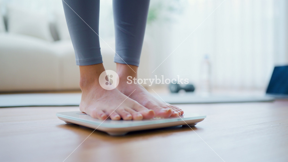 Closeup of feet, Young Asian woman standing on scales to measure her weight at home, Checking result of her slimming diet. Healthy living concept