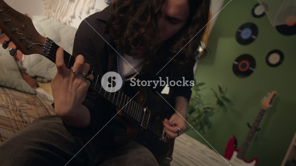 Dutch angle shot of young man playing electric guitar in bedroom, practicing chords and strumming. Clip for music education ads, creative hobby promos, or instrument marketing campaigns