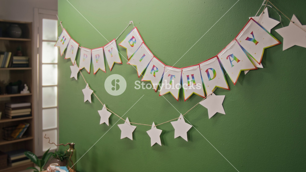 No people view of festive happy birthday garland on green-coloured wall of cozy living room with floor lamp and bookcase in background