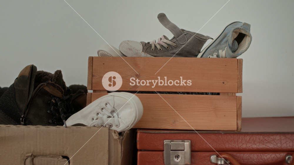 Close up no people shot of sneakers, boots, and low-top shoes, haphazardly stored in cardboard boxes and on wooden crates