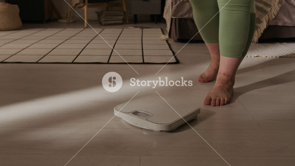 Plus-size Caucasian young adult woman stepping on floor scale to weigh herself at home. Footage is ideal for body positivity campaigns, weight loss tracking apps, and mental wellbeing content