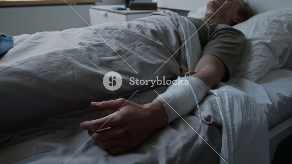 Caucasian man lying in hospital bed with IV drip in bandaged arm, resting. Footage for medical insurance advertising or healthcare services promotion
