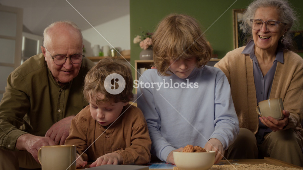 Handheld shot of Caucasian grandparents smiling while watching children solving jigsaw puzzle at home. Clip is ideal for family bonding, retirement lifestyle, and senior care commercial campaigns