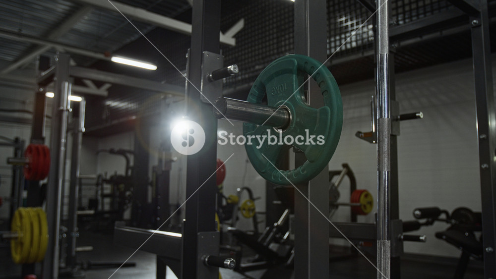 Barbell rack with green weight plate standing in empty gym interior. Footage for fitness center advertisements or health club marketing campaigns