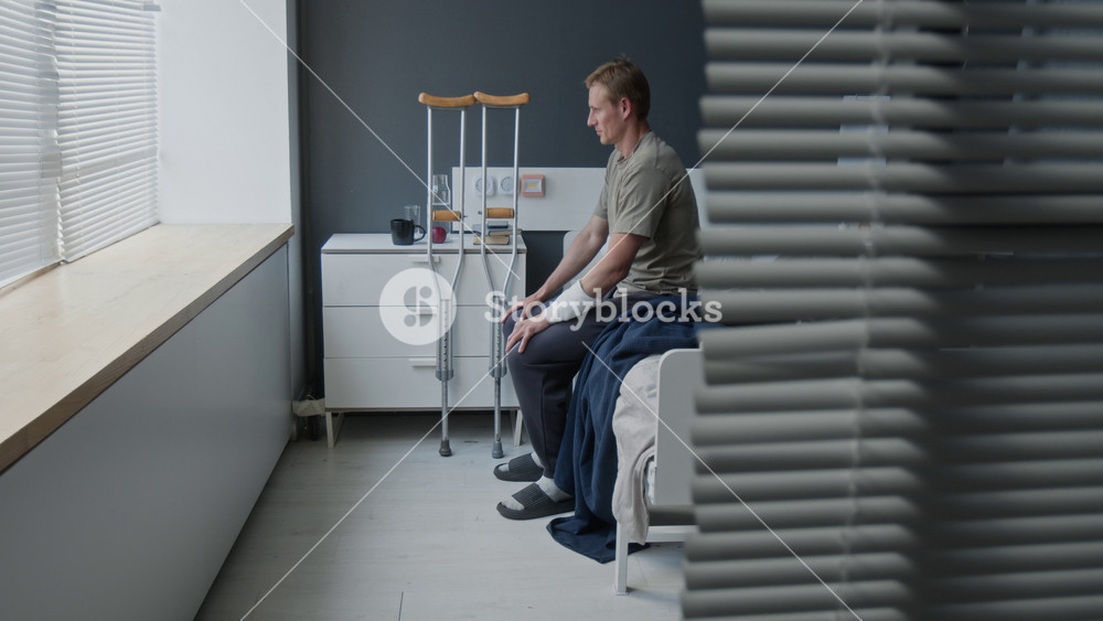 Young adult Caucasian man with bandaged arm standing up from hospital bed and walking with crutches. Clip for medical insurance, rehabilitation services, or healthcare marketing