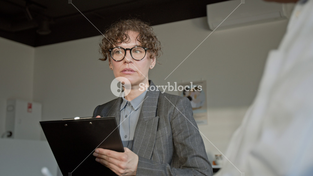 Rack focus shot of Caucasian female psychotherapist holding clipboard, speaking to female client during therapy session. Clip for mental health campaigns or counseling services