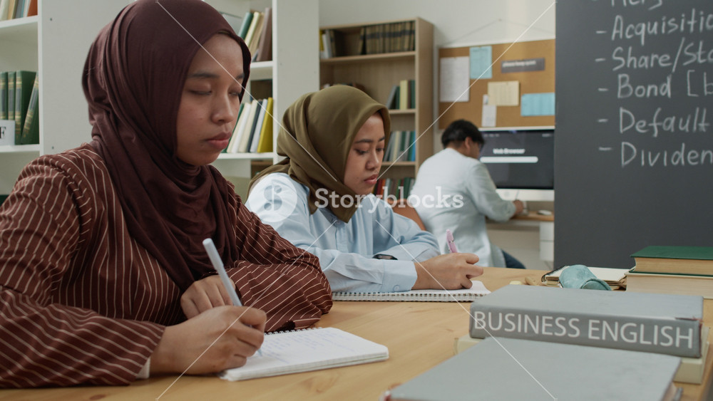 Young adult Asian female students wearing hijabs taking notes during Business English class in library. Clip is perfect for marketing campaigns on adult education, diversity, and language learning