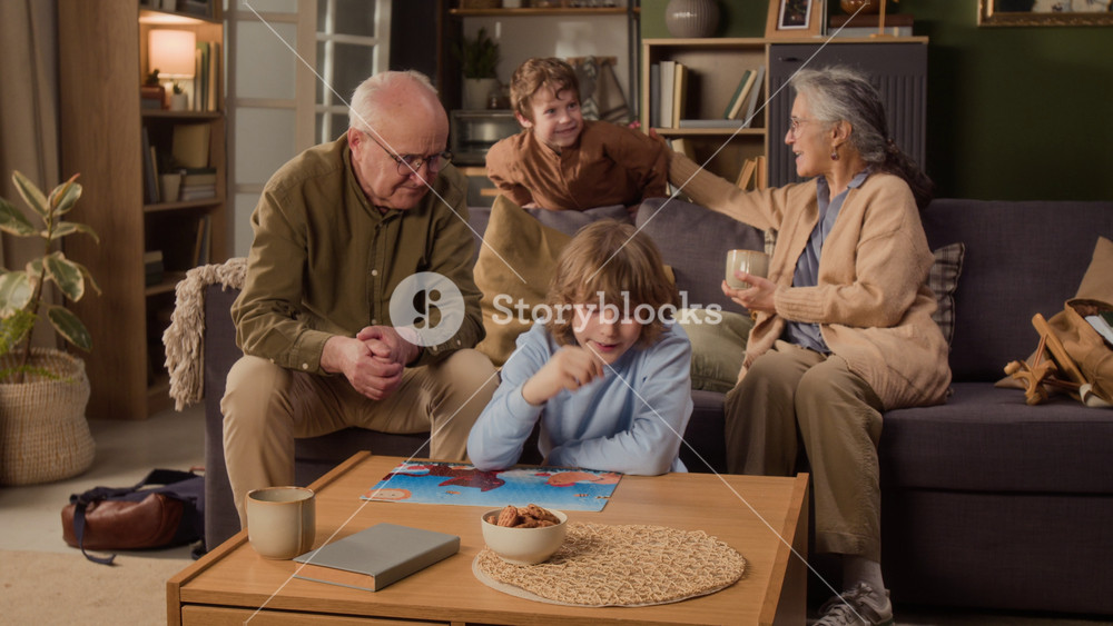 Long shot of grandparents sitting on sofa with grandsons completing puzzle and celebrating with high five. Footage ideal for retirement planning, family bonding, or educational toy commercials