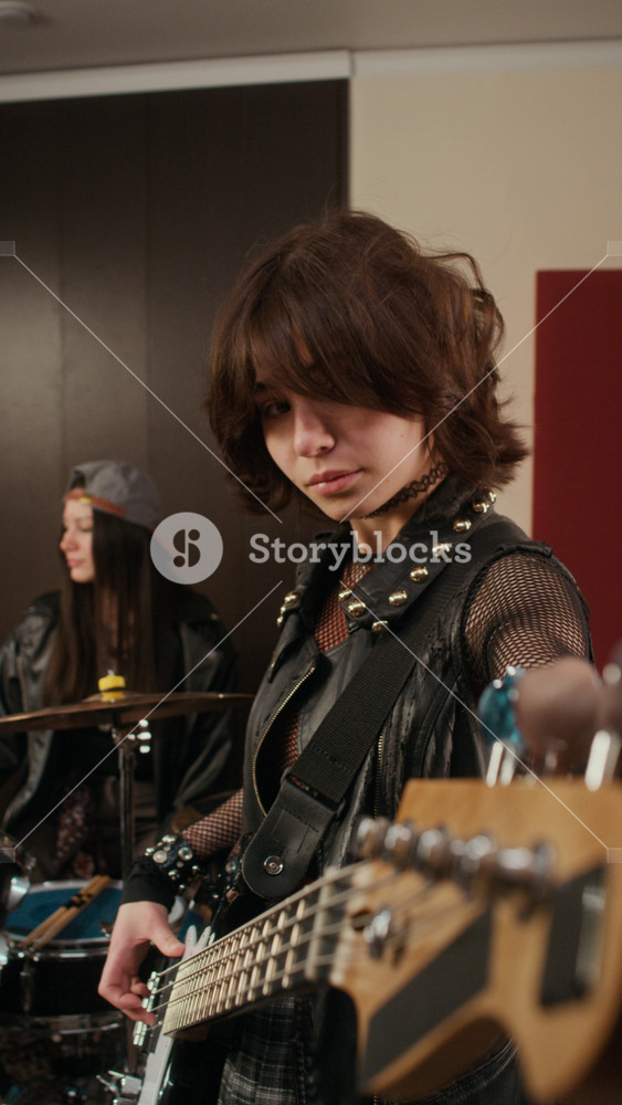 Vertical shot of Caucasian female teenager tuning bass guitar during rock band rehearsal in studio. Video is suitable for music school advertisements and youth hobby marketing campaigns