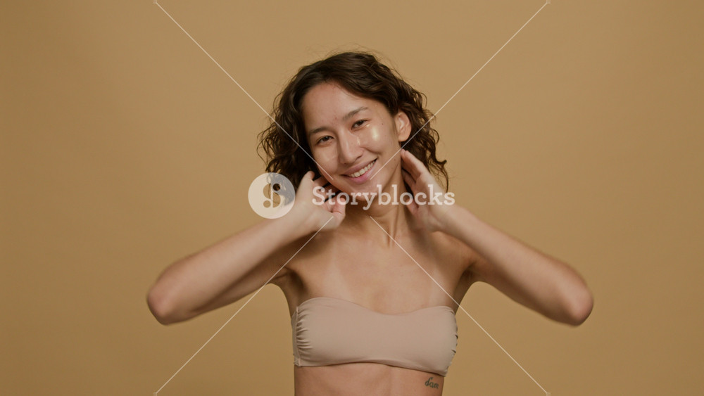 Waist-up studio portrait of cheerful Caucasian young woman in tube top with under eye patches smiling for camera against plain background