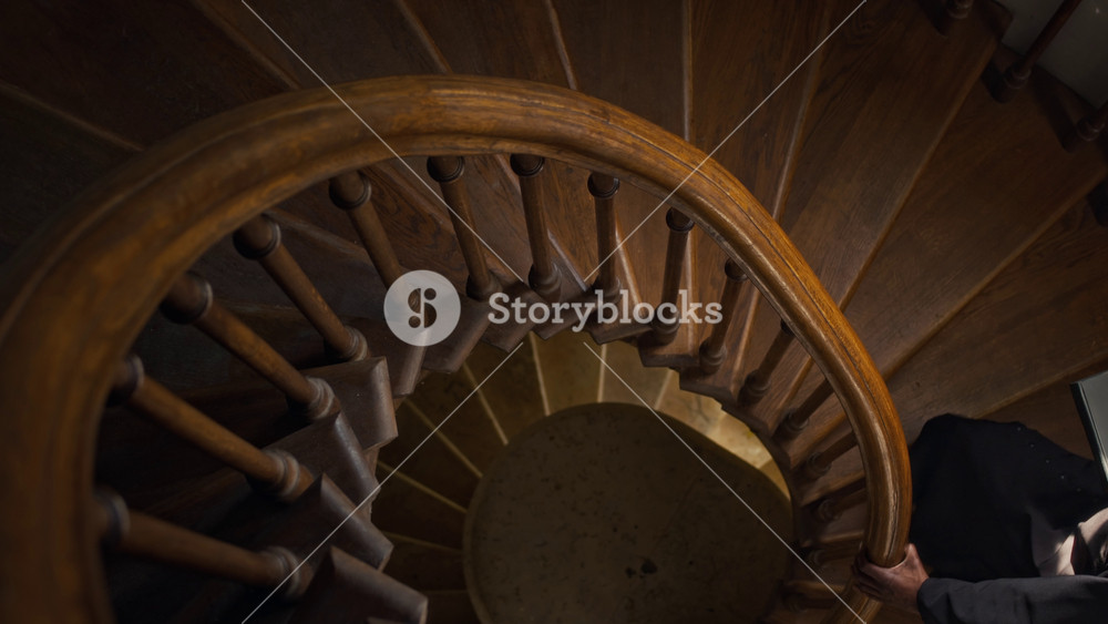 High angle view of African American catholic priest with holy bible going up wooden stairs holding winding banister in church