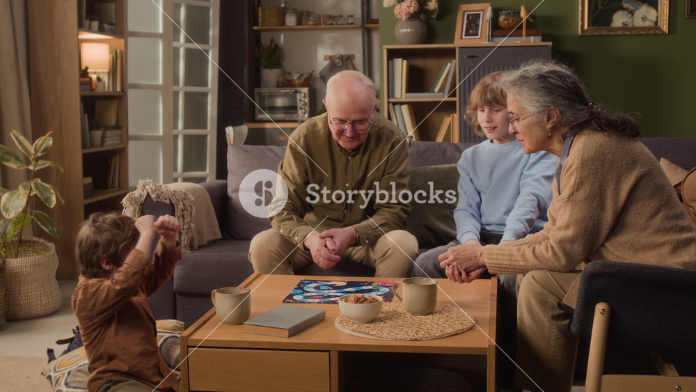 Long shot of senior Caucasian grandparents playing board game with young grandsons in living room. Clip showcases multigenerational family bonding, perfect for retirement planning or toy commercials