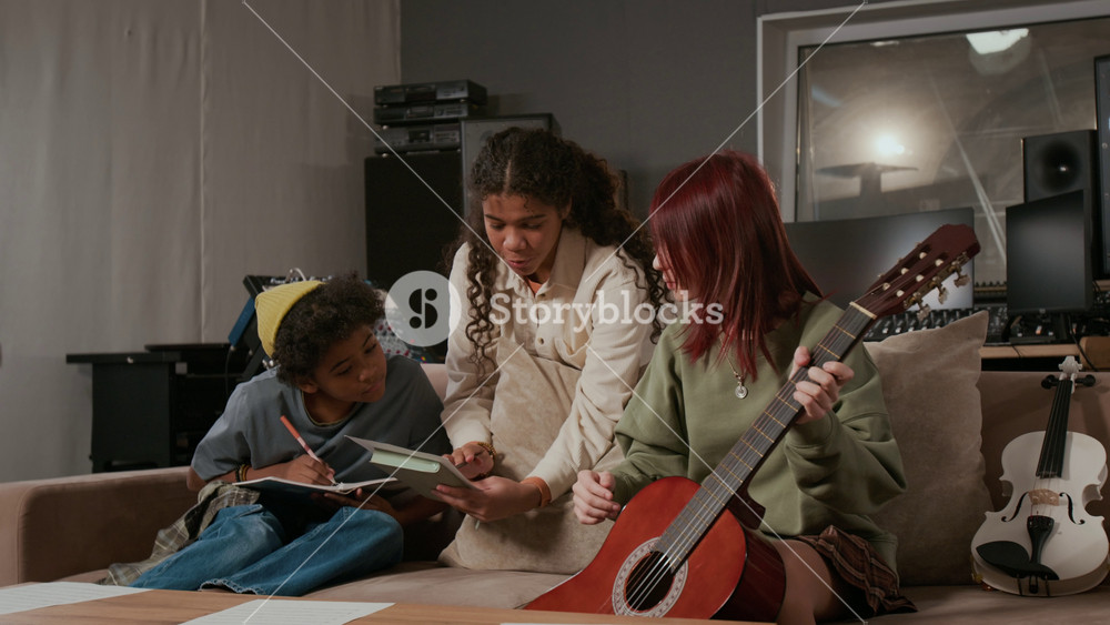 Positive adolescent girl suggesting lyrics for new song to teenage singer and guitar player during band rehearsal in music recording studio
