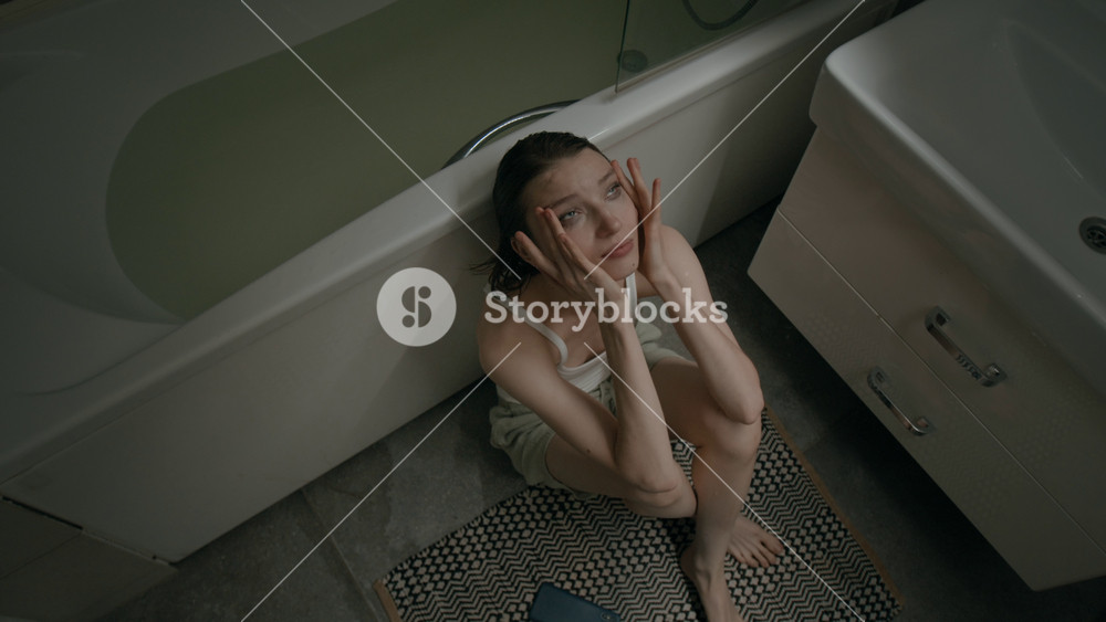 High angle zoom in shot of gen Z girl dressed in tank top and shorts touching face with hands when suffering from anxiety in bathroom