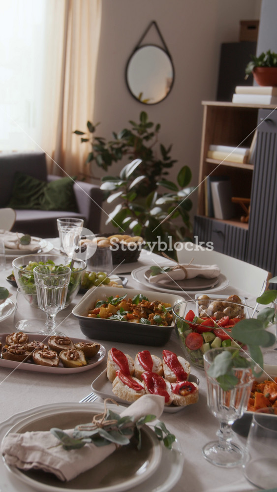 Vertical no people view of holiday table with white cloth displaying delicious dishes and starters, glassware and plates with napkins set for family dinner in living room