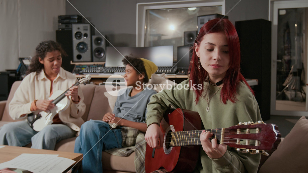 Caucasian red-haired teenage guitarist rehearsing song with African American adolescent violinist and singer in music recording studio