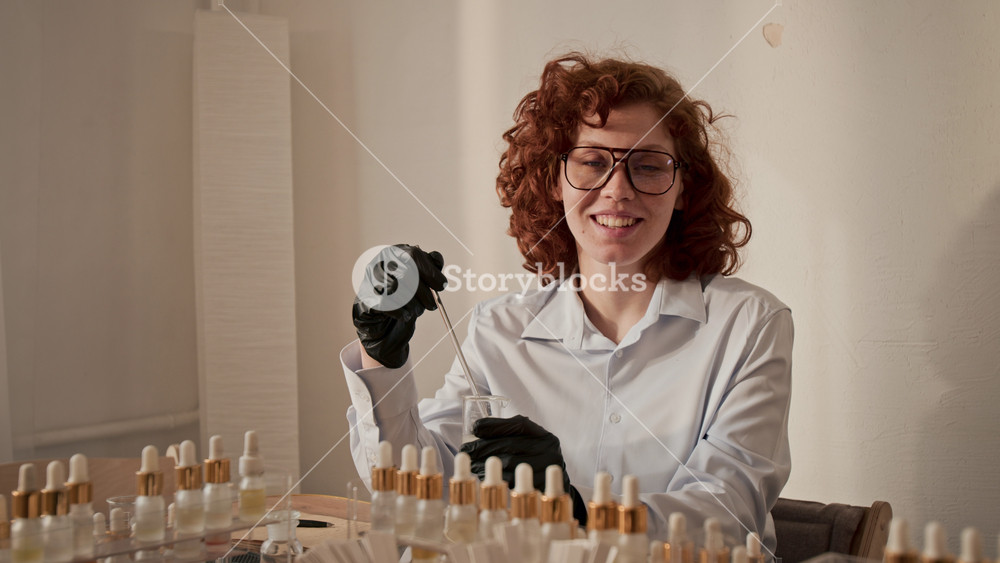 Portrait of Caucasian young adult woman smiling at camera while holding pipette in beaker during perfumery master class. Clip is perfect for beauty brand promo or cosmetic workshop ad