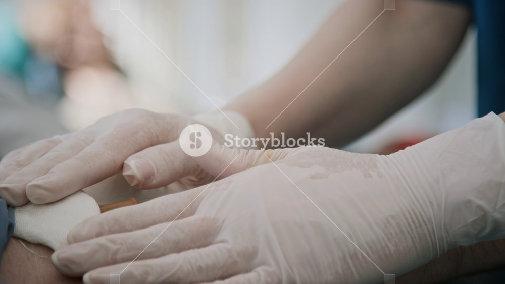 Close-up shot of unrecognizable nurse in gloves and blue scrubs putting bandage onto arm of man, donating his blood in clinic