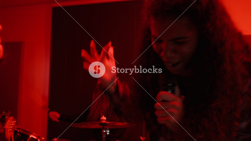 African American female teenager singing into microphone during rock band rehearsal with Caucasian drummer in background. Footage ideal for youth culture and music school promotions