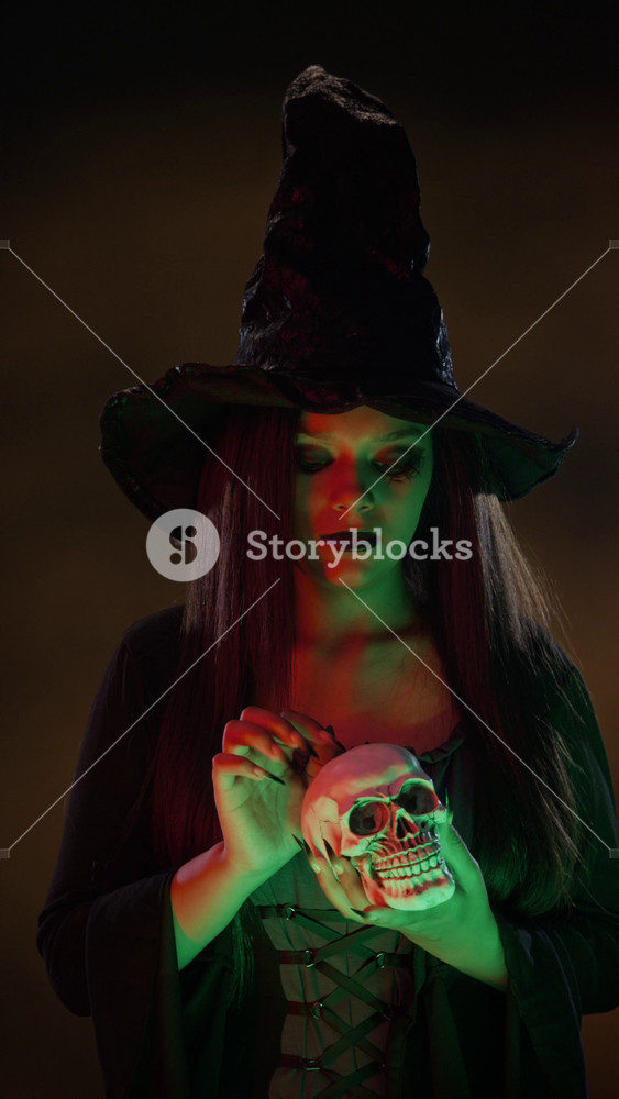 Portrait of girl in dressed as witch holding skull, looking at camera and stroking prop. Perfect for Halloween marketing campaigns or spooky event promotions, vertical