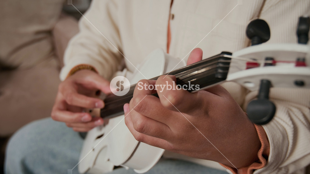 Close-up view of unrecognisable teenage girl wearing jeans and white cardigan playing violin without bow during music rehearsal