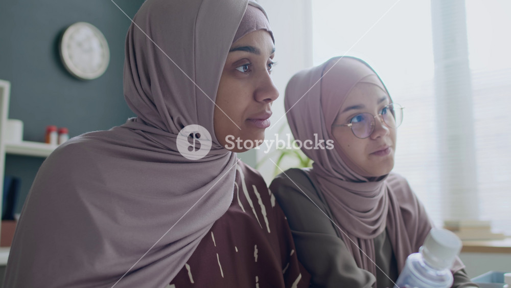 Tilt-up shot of Muslim mother and daughter in hijabs examining pills given by doctor and asking questions in clinic