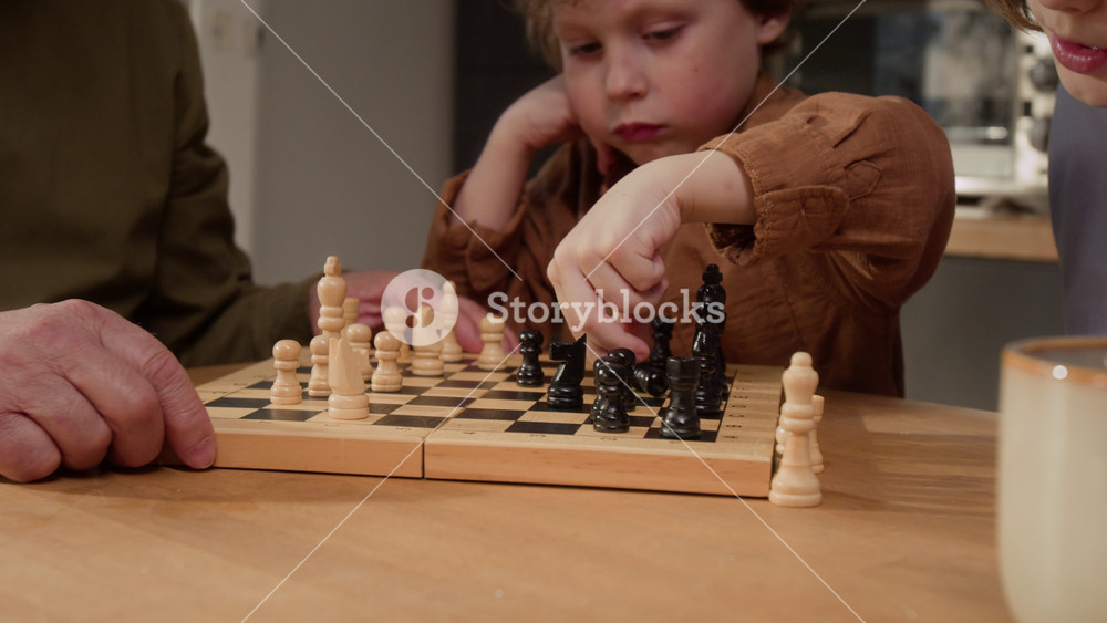 Medium close up shot of senior man and children playing chess at home, moving wooden pieces on board. Clip is ideal for family bonding, intergenerational learning, and educational game promotions