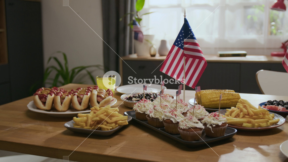 No people shot of wooden table laid for independence day celebration with hamburgers, corn, fries, cupcakes, hot dogs and glasses of juice