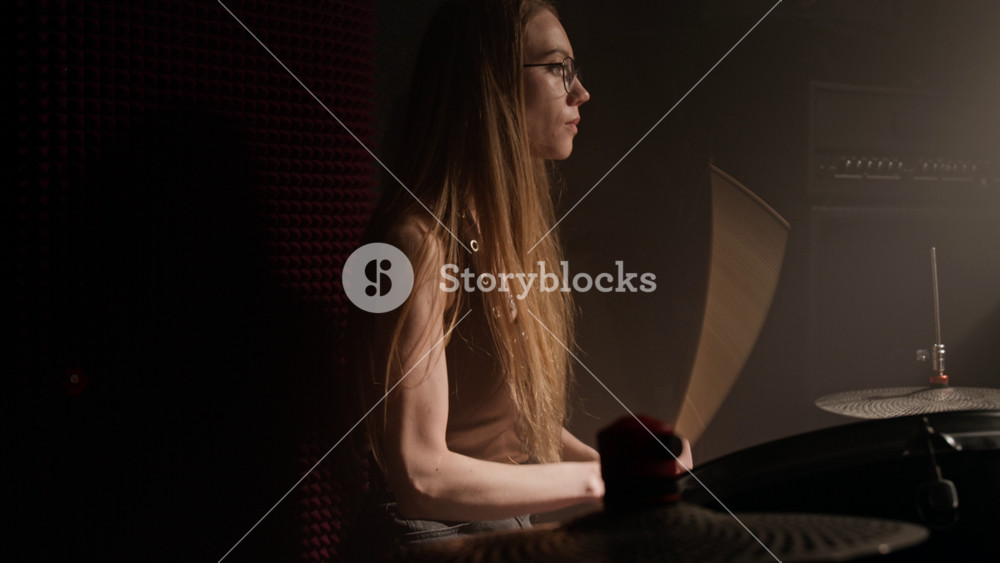Caucasian young female musician playing drums with drumsticks in rehearsal room. Footage for music school advertisements, band promotions, and creative lifestyle campaigns