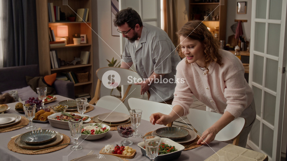 Caucasian family preparing dining table for dinner, young woman arranging food while child and man setting up chairs. Ideal for family lifestyle and holiday gathering commercials