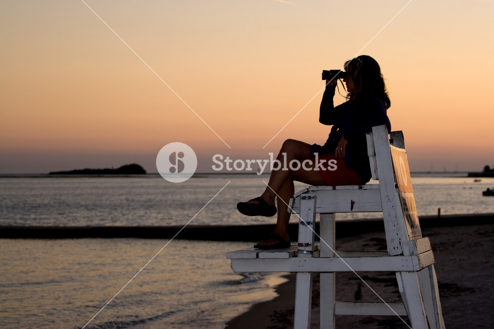A silhouette of a woman looking with binoculars at the beach while ...