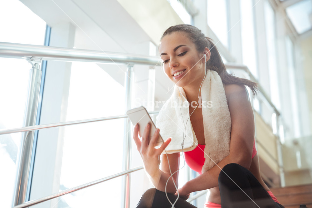 Joyful young woman enjoying music while sitting on gym stairs