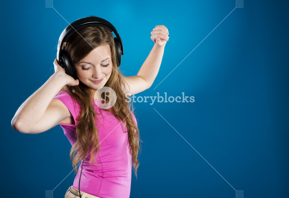 Teenage girl with headphones on blue background, enjoying music.