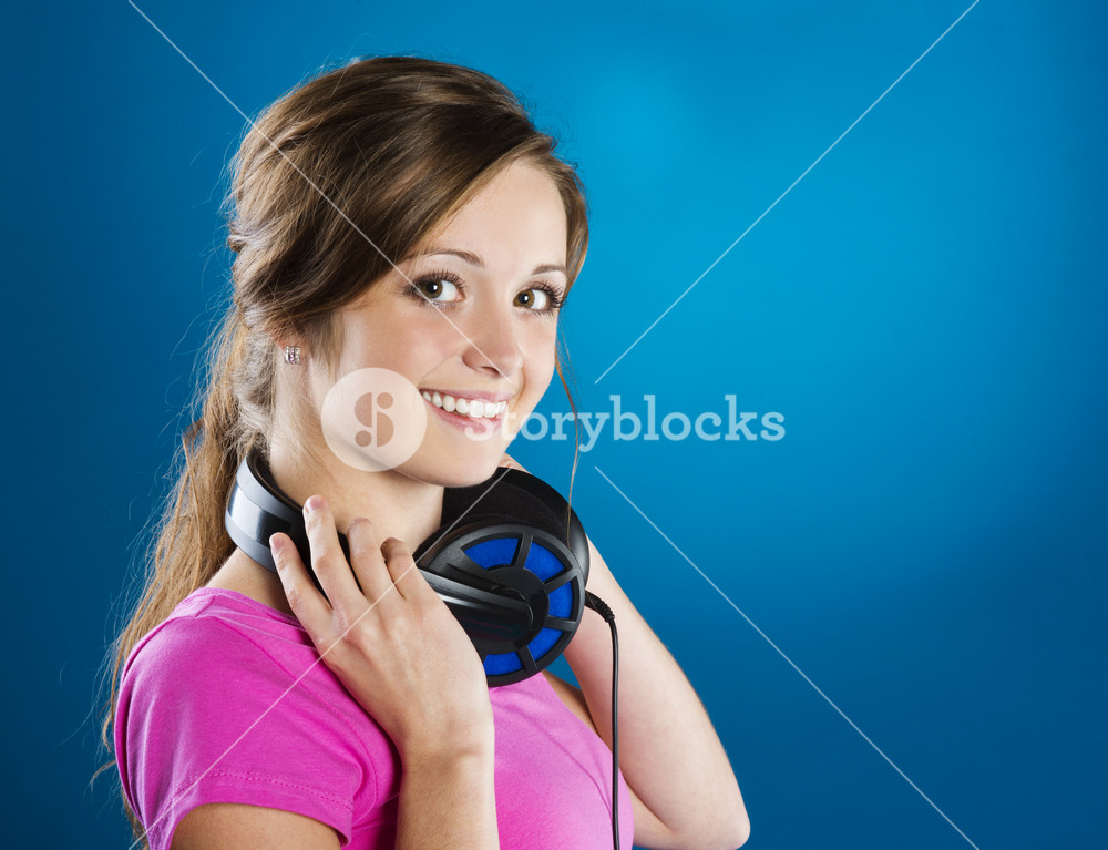 Teenage girl with headphones on blue background, enjoying music.