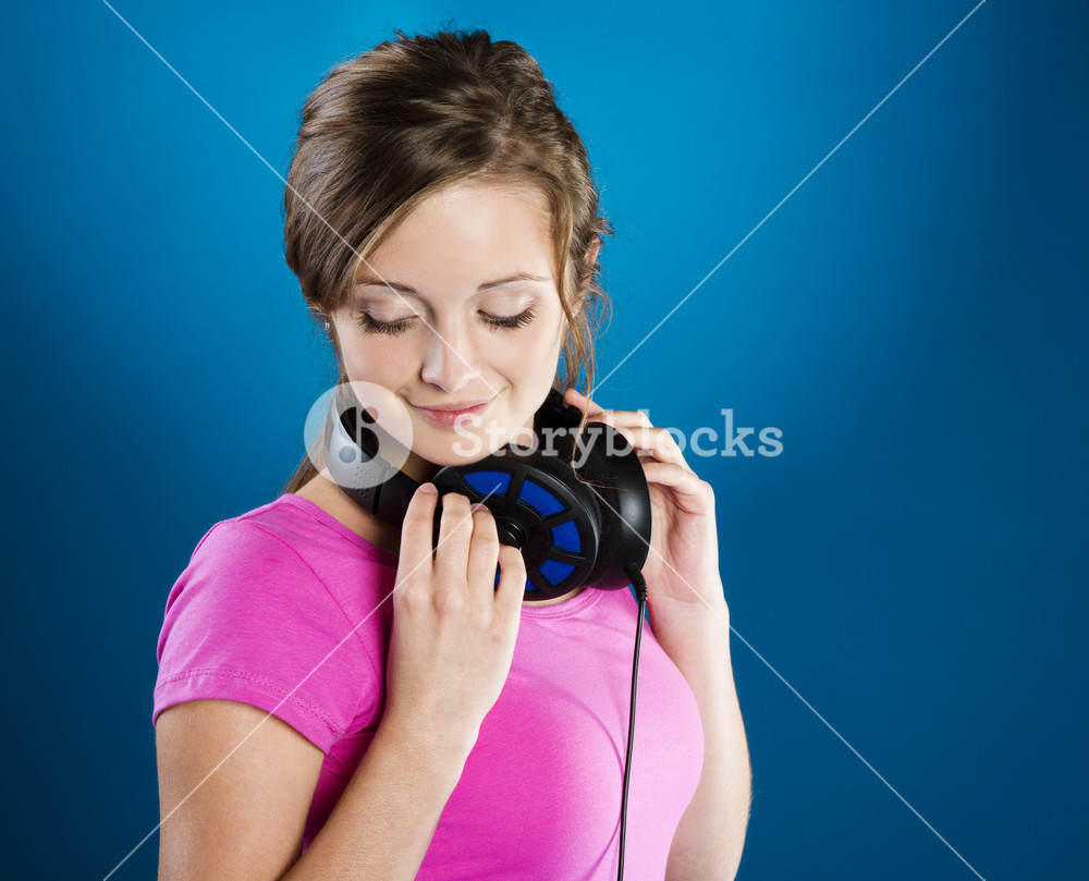 Teenage girl with headphones on blue background, enjoying music.