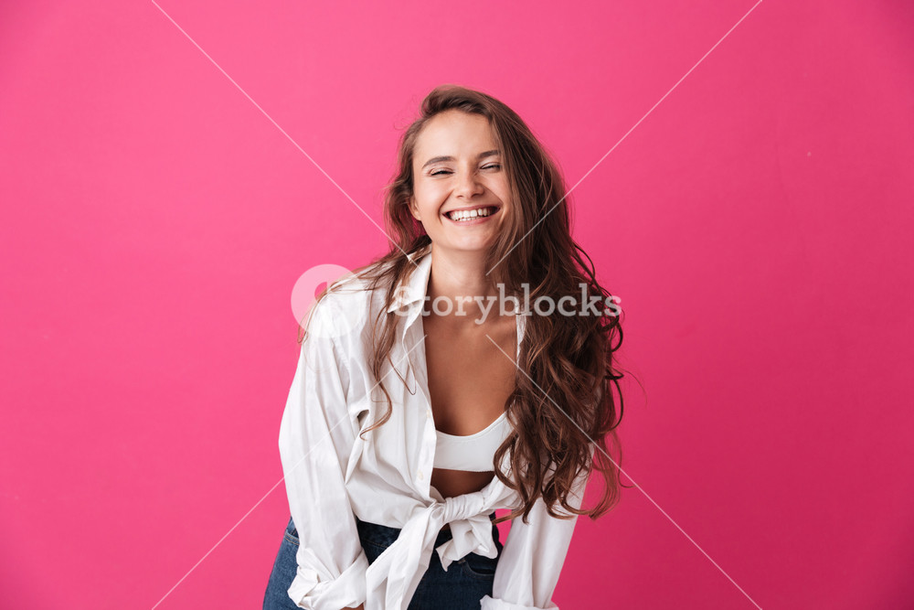 Young woman with curly hair smiling and looking at camera on pink ...