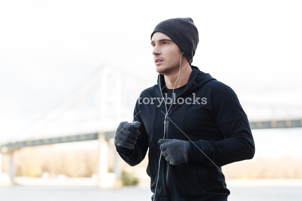 Young male athlete enjoying music while running outdoors