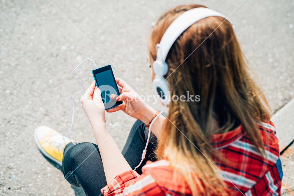 Young woman listening to music with headphones and smartphone in the city - music, technology, communication concept
