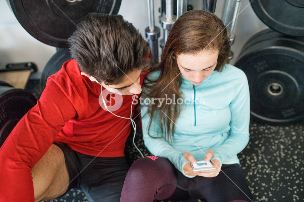Fit couple in modern gym resting, using smart phone