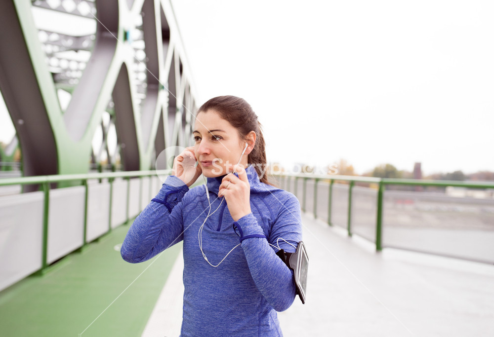 Young woman with smartphone and earphones, enjoying music while running on a green steel bridge in the city.