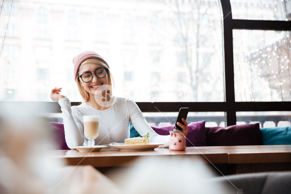 Joyful young woman enjoying music on her phone and laughing at a cafe